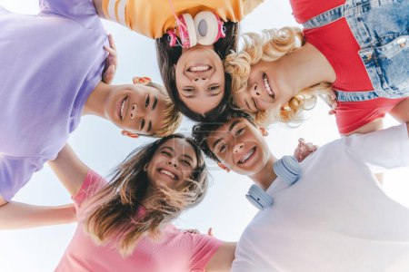 Foto de Grupo de adolescentes multirraciales felices, amigos sonrientes con camisetas de colores abrazando, mirando a la cámara en la calle. Niños y niñas de escuela positiva de pie juntos. Amistad, vacaciones, verano - Imagen libre de derechos