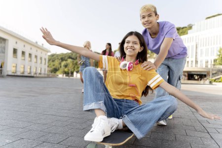 Téléchargez les photos : Portrait d'amis adolescents souriants assis, chevauchant sur skateboard dans la rue urbaine. Groupe de garçons et de filles heureux multiraciaux s'amuser ensemble. Vacances scolaires, été, concept de style de vie positif - en image libre de droit