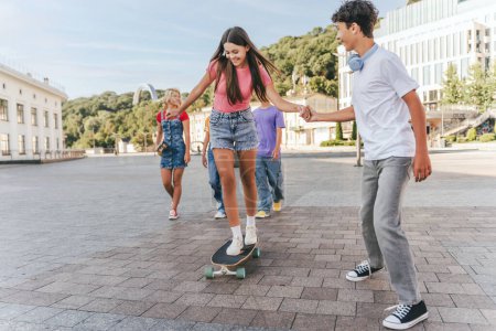 Photo for Portrait of happy, attractive teenagers, friends having fun, skateboarding on urban street. Group of multiracial college students walking while meeting outdoors. Friendship, positive lifestyle concept - Royalty Free Image