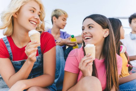 Photo for Group of happy friends, multiracial teenagers eating ice cream, talking sitting on the street. Happy stylish boys and girls communication outdoors, having fun. Friendship, positive lifestyle, summer - Royalty Free Image