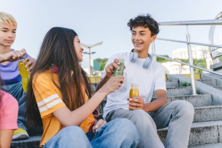 Photo for Group of happy teenage friends, drinking lemonade talking sitting on stairs. Happy stylish boys and girls communication on the street. Friendship, summer holidays concept - Royalty Free Image
