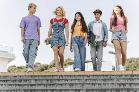 Photo for Smiling, attractive teenagers wearing stylish colorful t shirts walking together on the stairs. College friends metting, communication. Concept of friendship - Royalty Free Image