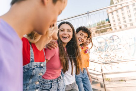 Foto de Retrato de adolescentes multirraciales sonrientes en camisetas coloridas, niños elegantes que se reúnen, comunicación al aire libre. Estudiantes universitarios modernos positivos caminando juntos por las calles urbanas de la ciudad - Imagen libre de derechos