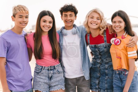 Photo for Group of smiling multiracial friends wearing colorful t shirts hugging each other standing on the street. Emotional stylish boys and girls looking at camera outdoors Friendship concept - Royalty Free Image
