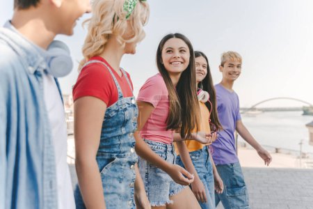 Photo for Group of smiling friends, multiracial teenagers wearing colorful casual clothes talking, walking on the street. Happy stylish boys and girls outdoors. Friendship, positive lifestyle, summer concept - Royalty Free Image