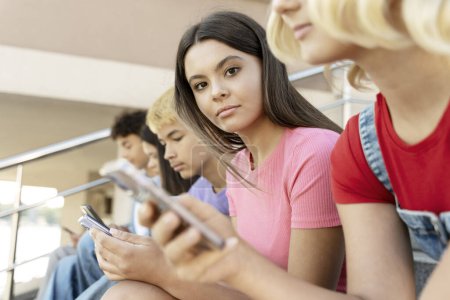 Photo for Group of serious multiracial teenagers using mobile phone, watching video communication online on the street. Portrait of sad girl holding smartphone looking at camera. Technology dependence - Royalty Free Image