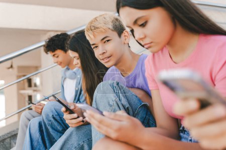 Photo for Portrait of smiling asian boy holding smartphone playing mobile game looking at camera. Group of multiracial teenagers using mobile phones, watching video communication online on street. Technology - Royalty Free Image