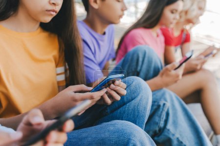 Photo for Group of serious multiracial teenagers holding mobile phones watching video, communication online, chatting, selective focus. Technology, social media concept - Royalty Free Image