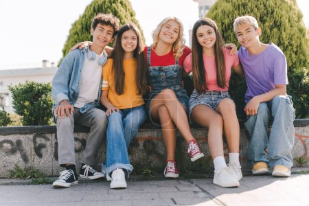 Photo for Portrait of positive happy teenagers sitting together, relaxing, hugging, looking at camera. Group of multiracial boys and girls in colorful t shirts. Vacation, positive lifestyle concept - Royalty Free Image
