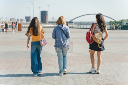 Photo for Rear view of attractive women in stylish casual clothes walking with backpack. Female with long hair in urban city. Concept of travel - Royalty Free Image