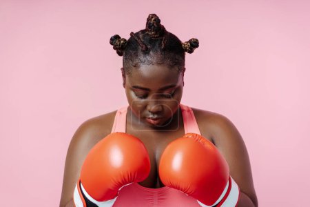 Téléchargez les photos : Boxeuse afro-américaine en gants de boxe rouge s'entraînant isolée sur fond rose. Femme séduisante faisant du sport, motivation, mode de vie sain concept - en image libre de droit