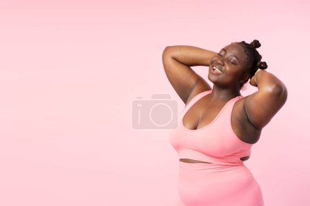 Téléchargez les photos : Portrait d'une jolie femme afro-américaine souriante portant un uniforme de sport posant pour une photo isolée sur fond rose, espace de copie. Belle plus la taille de la formation féminine, concept de fitness - en image libre de droit