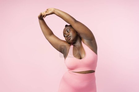 Photo for Beautiful modern plus size woman with stylish hairstyle wearing pink sports bra doing exercises isolated on pink background. Body positive female model, health care concept, motivation concept - Royalty Free Image