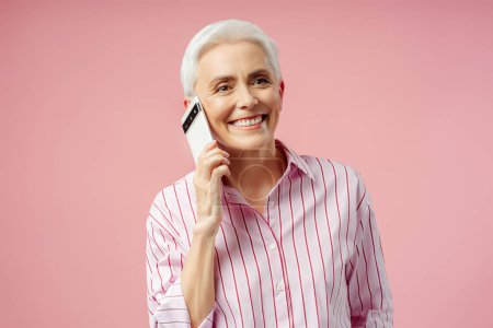 Téléchargez les photos : Femme âgée souriante, entrepreneur, gestionnaire parlant sur téléphone mobile isolé fond de studio rose. Portrait de smartphone d'appel freelance moderne - en image libre de droit