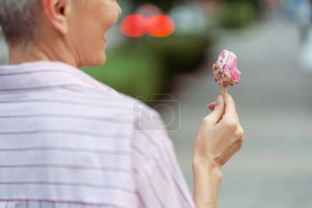Photo for Close up view of the happy stylish gray haired woman eating tasty ice cream while enjoying walk in park. Positive lifestyle and tasty food concept - Royalty Free Image