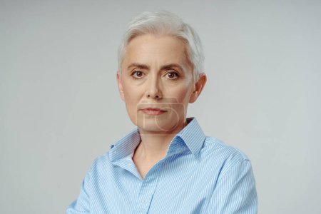 Photo for Portrait Caucasian attractive confident gray haired senior businesswoman looking at camera with serious face, standing over isolated grey background - Royalty Free Image