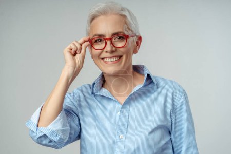 Photo for Authentic portrait of smiling senior woman wearing stylish red eyeglasses isolated on grey background, vision concept. Attractive happy gray haired businesswoman, confident manager looking at camera - Royalty Free Image