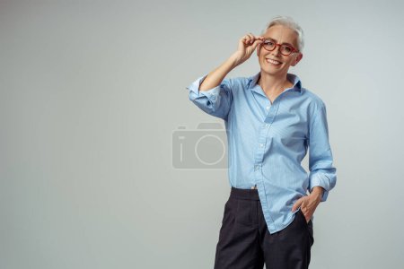Foto de Retrato de una mujer mayor sonriente con gafas rojas con estilo mirando a la cámara en el fondo gris. Concepto de negocio exitoso - Imagen libre de derechos