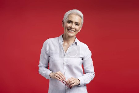 Photo for Smiling confident female teacher wearing casual shirt, holding glasses looking at camera. Successful businesswoman isolated on red mauve background, copy space - Royalty Free Image