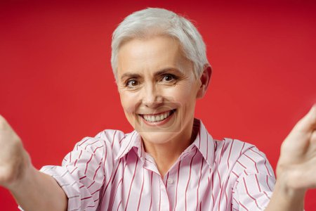 Téléchargez les photos : Portrait heureux poil gris gai femme d'affaires senior regardant la caméra et faisant selfie debout sur fond gris isolé - en image libre de droit