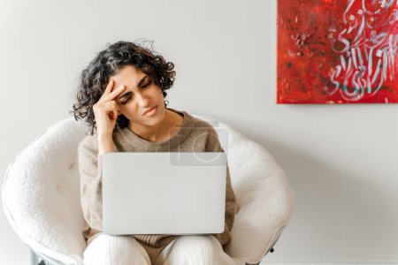 Photo for Tired curly woman using laptop computer, studying, learning language. Serious student searching information, working online sitting at home. Education concept - Royalty Free Image