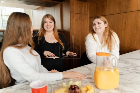 Téléchargez les photos : Joyeux dames boire du jus et manger des collations, profiter du temps ensemble à la maison. Femmes gaies passer du temps ensemble - en image libre de droit