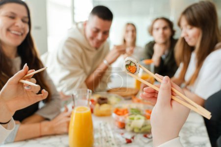 Foto de Vista recortada de los colegas de la gente sosteniendo palos de madera, disfrutando de sushi con bebidas mientras celebran cumpleaños juntos - Imagen libre de derechos