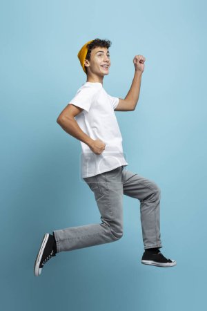 Téléchargez les photos : Portrait de beau garçon sur des vêtements décontractés, sautant, isolé sur fond bleu, regardant la caméra - en image libre de droit