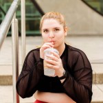 Plus size woman in sportswear drinking water while sitting on the steps outdoors. Body positive, sport, motivation