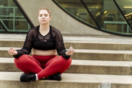 Photo for Plus size female in sportswear meditating with eyes closed on the stairs. Outdoor workout. Healthy active lifestyle concept - Royalty Free Image
