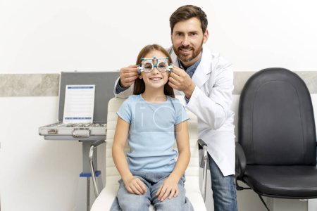Téléchargez les photos : Bonne petite fille portant un cadre d'essai optométriste à la clinique d'ophtalmologie. Soins de santé, médecine, concept de diagnostic - en image libre de droit