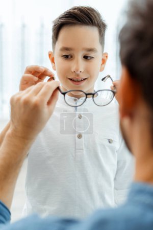 Foto de Un joven dando gafas para un niño en la óptica. Concepto de salud - Imagen libre de derechos