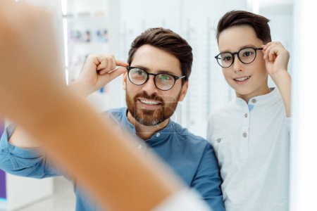 Photo for Smiling father and little son wearing glasses, posing in optical shop. Health care concept - Royalty Free Image