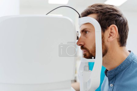 Téléchargez les photos : Un bel homme assis dans une armoire optométriste et qui fait vérifier sa vue. Concept diagnostique - en image libre de droit