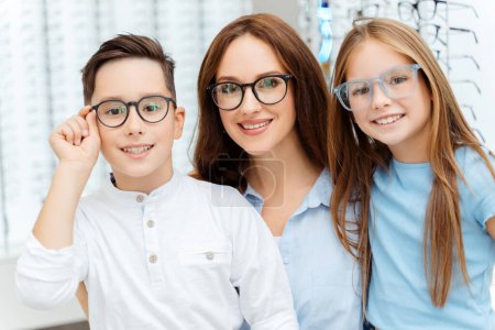 Photo for Smiling mother with little son and daughter posing in optical store while choosing glasses. Health care, family concept - Royalty Free Image