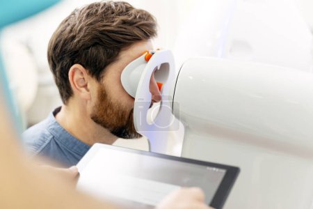 Foto de Un joven que se hace la prueba de la vista, usando un refractómetro moderno, mirando dentro de la máquina. Diagnóstico, concepto de atención médica - Imagen libre de derechos