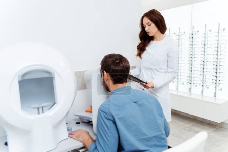 Foto de Médico oftalmólogo femenino en laboratorio óptico de examen con paciente masculino. Diagnóstico, concepto de atención médica - Imagen libre de derechos