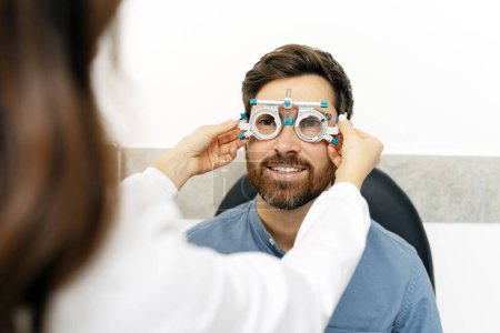 Téléchargez les photos : Optométriste féminine vérifiant la vision à l'œil pour l'homme dans une clinique moderne. Soins de santé, médecine, concept humain - en image libre de droit