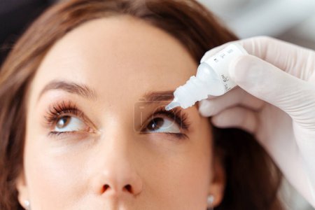 Foto de Optometrista poniendo gotas para los ojos en los ojos de la paciente femenina para una visión clara. Concepto de salud - Imagen libre de derechos