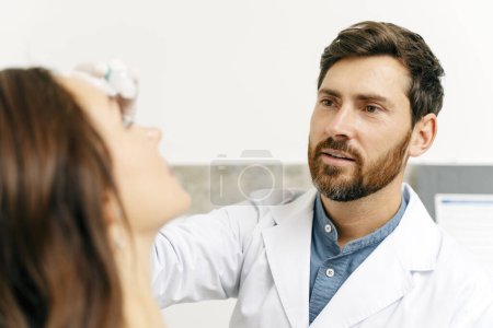 Foto de El atento optometrista masculino gotea gotas en los ojos del paciente. Concepto de salud - Imagen libre de derechos