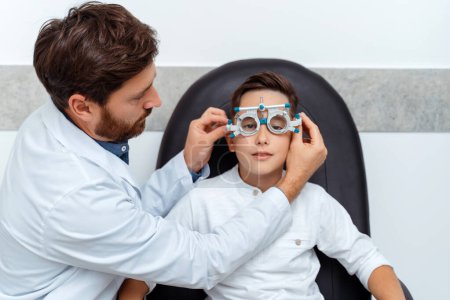 Téléchargez les photos : Ophtalmologiste masculin examinant petit garçon tout en ajustant le nombre de monture de lentille. Soins de santé, médecine, concept de diagnostic - en image libre de droit