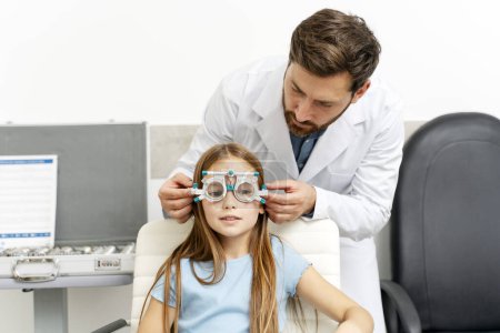 Téléchargez les photos : Médecin tenant un équipement oculaire spécial tout en examinant les yeux de fille dans la clinique ophtalmologique. Soins de santé, médecine, concept de diagnostic - en image libre de droit