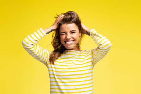 Téléchargez les photos : Portrait d'une femme souriante joyeuse jouant avec ses cheveux, s'amusant, regardant la caméra isolée sur fond jaune. Concept de mode de vie positif - en image libre de droit