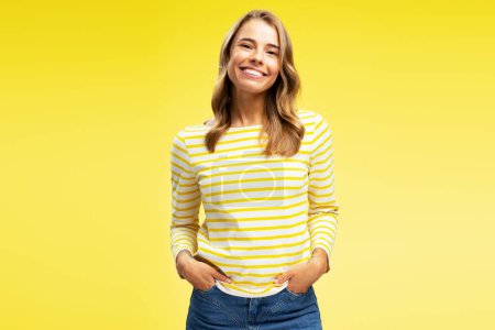 Téléchargez les photos : Portrait de heureuse belle Américaine portant des vêtements décontractés regardant la caméra debout isolé sur fond jaune. Concept de publicité - en image libre de droit