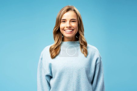 Photo for Smiling attractive woman wearing cozy sweater looking at camera standing isolated on blue background. Concept of beauty, makeup - Royalty Free Image