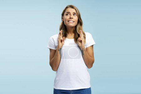 Photo for Portrait of young woman wearing casual clothes with crossed fingers standing isolated on blue background looking at camera. Concept of wish something, hope - Royalty Free Image