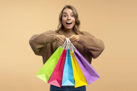 Téléchargez les photos : Jeune belle femme excitée portant des sacs à provisions colorés regardant la caméra isolée en arrière-plan. Shopping, vendredi noir, vente, concept publicitaire - en image libre de droit