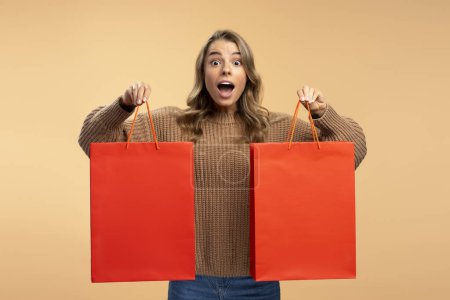 Téléchargez les photos : Femme excitée tenant des sacs à provisions rouges regardant la caméra isolée en arrière-plan, maquette. Shopping, vendredi noir, vente, concept publicitaire - en image libre de droit