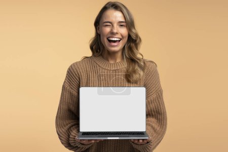 Téléchargez les photos : Belle femme souriante clins d'oeil tenant ordinateur portable montrant écran d'ordinateur isolé sur fond, maquette. Portrait de jeune étudiant heureux étudiant, apprendre la langue, concept d'éducation en ligne. Technologie - en image libre de droit