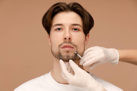 Photo for Cosmetologist in gloves making beauty injection for young man. Isolated on beige background. Beauty care, anti aging procedures, plastic surgery concept - Royalty Free Image